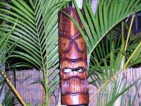 Tiki carving in front of Palm fronds and a bamboo fence